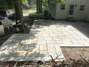 Backyard patio installation with natural stone pavers near house and trees.