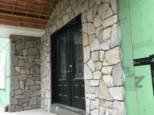 Stone veneer installation around black double front doors.