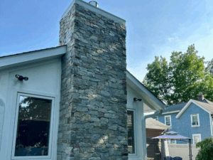 Stone chimney installation on white modern house exterior.