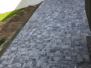 Backyard paver patio installation showing interlocking concrete pavers arranged in a uniform pattern on a leveled outdoor surface