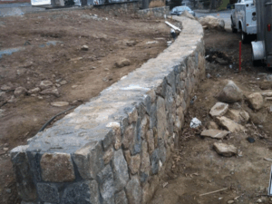 Stone retaining wall construction in progress on sloped residential terrain.