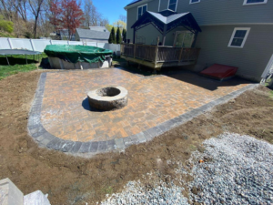 Brick paver patio with integrated fire pit installed in a residential backyard, showing curved edges and completed paver surface.