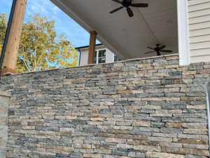 Stacked stone retaining wall construction supporting elevated porch with natural stone masonry finish