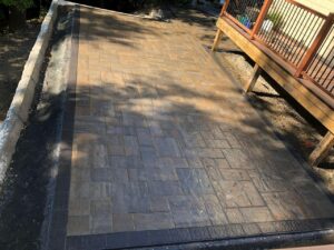 Completed stone paver patio installation alongside elevated deck structure