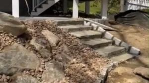 Close view of a boulder retaining wall filled with river rock next to a house.